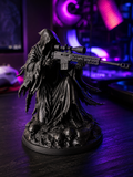 3D printed matte black Grim Reaper statue aiming a scoped sniper rifle, standing on a base of skulls